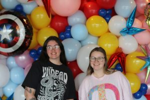 2 suretybonds.com transaction coordinators posing in front of a balloon backdrop from a company event